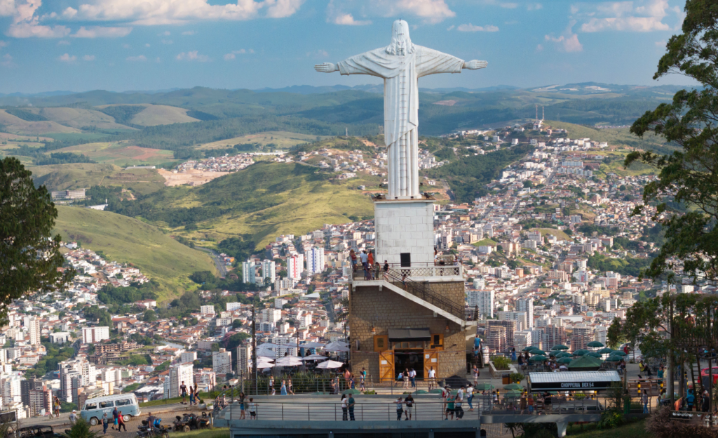 Guia Completo do Teleférico de Poços de Caldas: História, Vista Panorâmica e Dicas de Visitação 3 Turistas desembarcando na estação do topo da Serra de São Domingos, com a estátua do Cristo Redentor ao fundo e céu azul