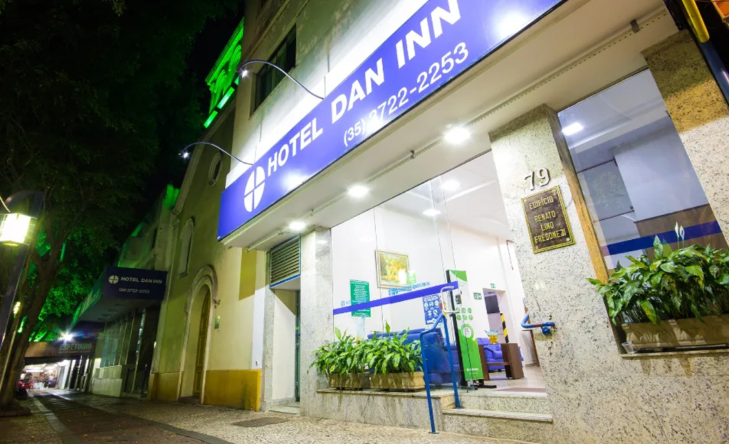 Fachada do Hotel Dan Inn Poços de Caldas localizada no centro comercial, destacando a proximidade com bancos e serviços urbanos