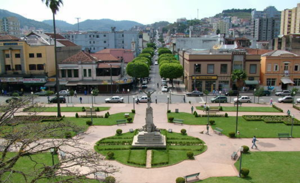 Hotel Dan Inn Poços de Caldas: O Guia Definitivo de Praticidade e Economia no Sul de Minas 3 Hóspedes caminhando tranquilamente na Praça Pedro Sanches, próxima ao Hotel Dan Inn Poços de Caldas, com o Palace Casino ao fundo