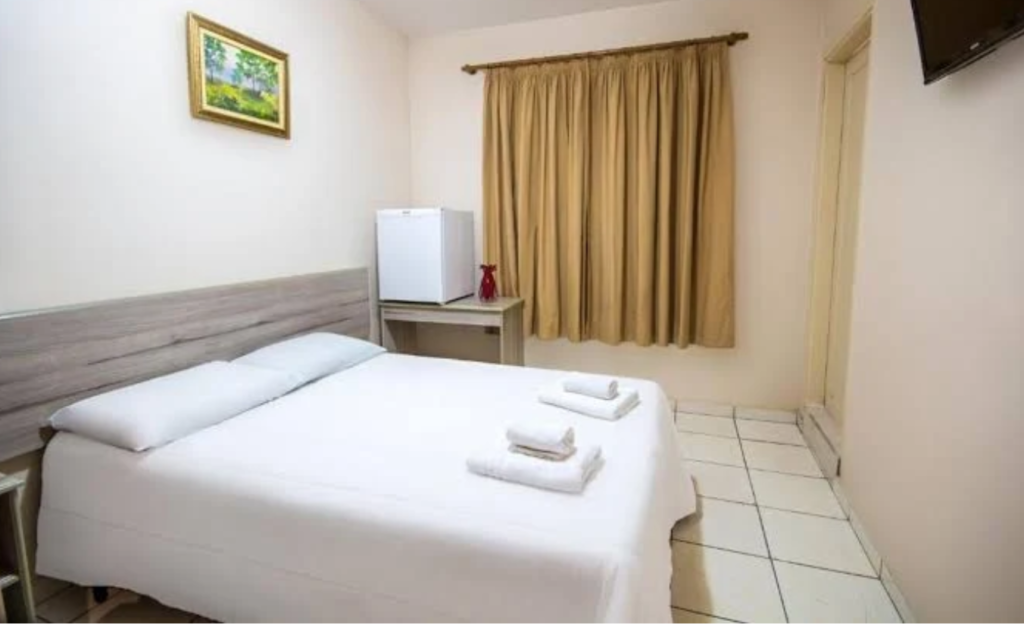 Hotel Dan Inn Poços de Caldas: O Guia Definitivo de Praticidade e Economia no Sul de Minas 4 Quarto confortável e organizado do Hotel Dan Inn Poços de Caldas, mostrando a cama e a iluminação acolhedora