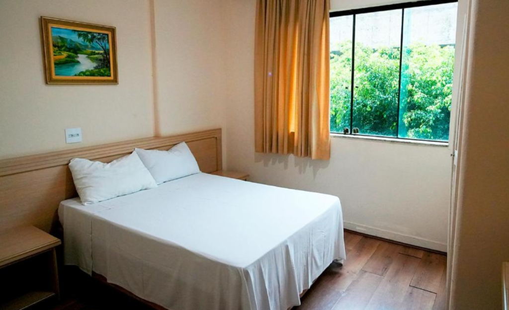 Hotel com sala de eventos em Poços de Caldas: infraestrutura que resolve para encontros corporativos até 80 pessoas 3 Quarto confortável do Dan Inn Poços de Caldas com cama arrumada, TV, frigobar e iluminação acolhedora para hóspedes em viagem corporativa