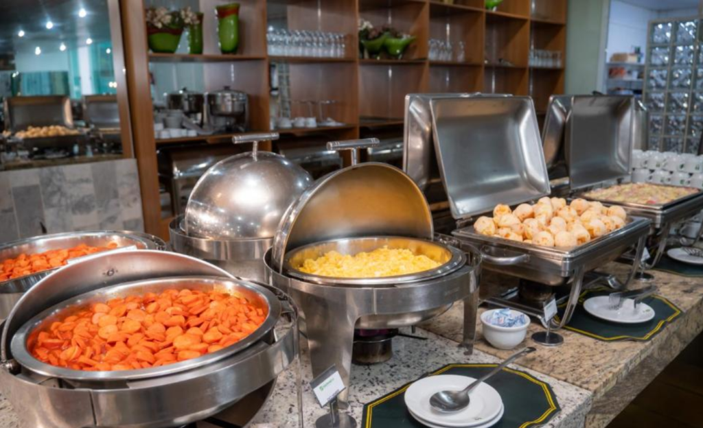 Conforto Mineiro para Eventos Corporativos em Poços de Caldas: tradição e funcionalidade no Nacional Inn 3 Mesa de café da manhã mineiro no Nacional Inn Poços de Caldas com queijos artesanais, pães caseiros, frutas e café servidos para participantes de evento corporativo
