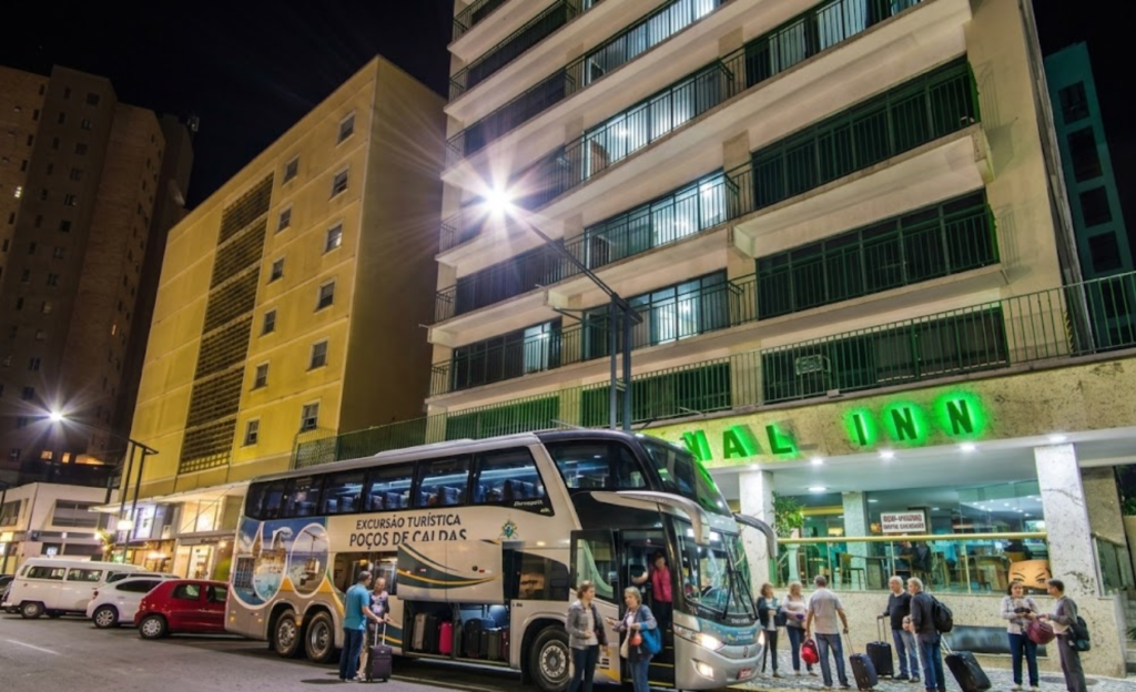 Excursão em Poços de Caldas: o guia completo para grupos que buscam tradição, conforto e roteiro inesquecível 4 Ônibus de excursão turística estacionado em frente ao Nacional Inn Poços de Caldas com grupo de viajantes desembarcando