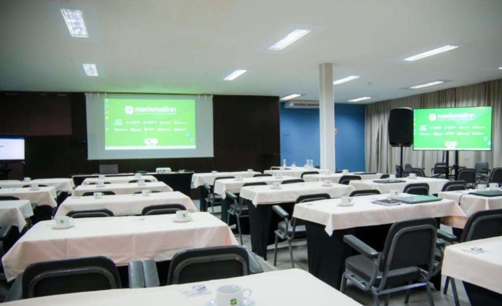 Conforto Mineiro para Eventos Corporativos em Poços de Caldas: tradição e funcionalidade no Nacional Inn 2 Salão de convenções do Nacional Inn Poços de Caldas preparado para evento corporativo com mesas organizadas e equipamentos audiovisuais