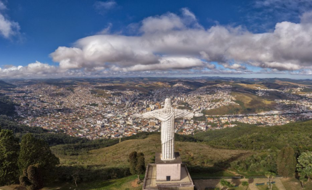 Excursão em Poços de Caldas: o guia completo para grupos que buscam tradição, conforto e roteiro inesquecível 2 Vista panorâmica de Poços de Caldas com o Cristo Redentor ao fundo e a cidade cercada pela Serra de São Domingos